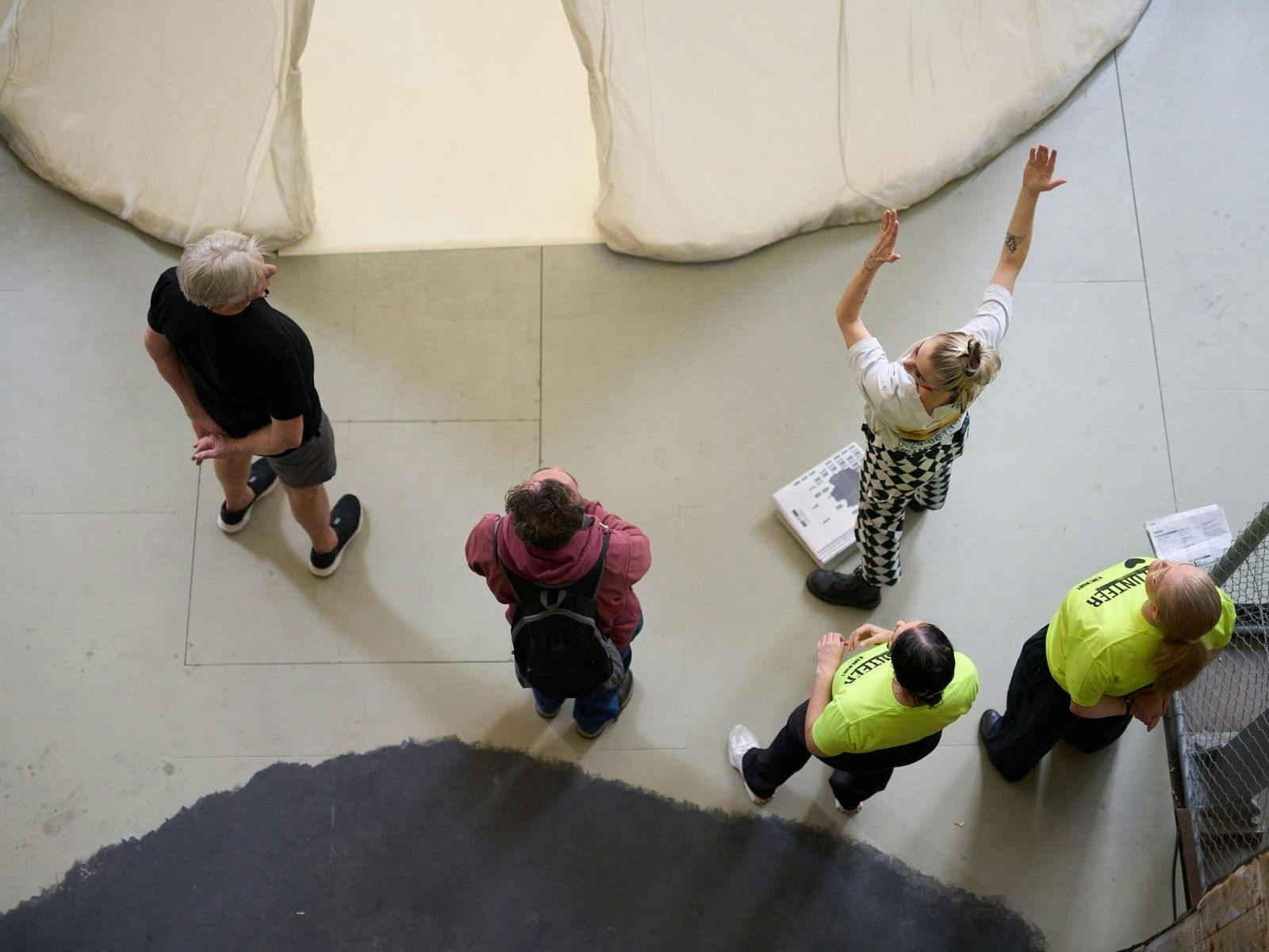 Tour guide gestures toward a large canvas artwork as tour attendess look at it