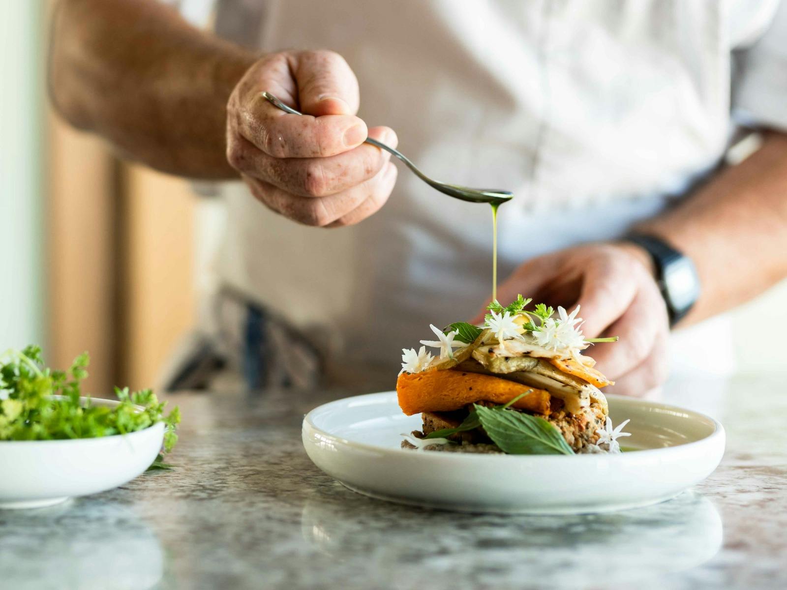 Chef plating Herbed chickpea fritter, baba ghanoush and grilled autumn vegetables