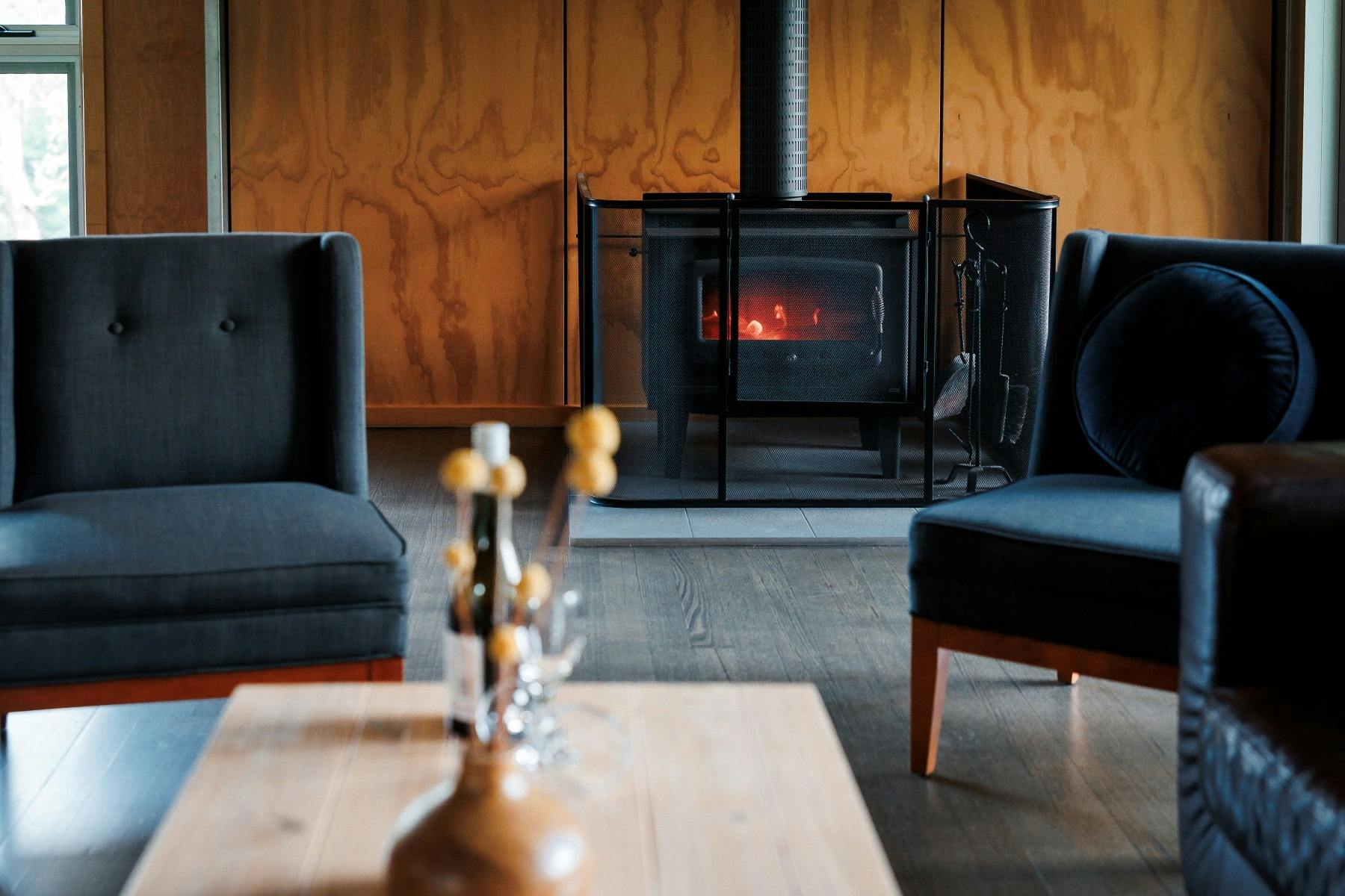Cosy room with ply walls, freestanding fireplace with fire going, two blue occasional chairs