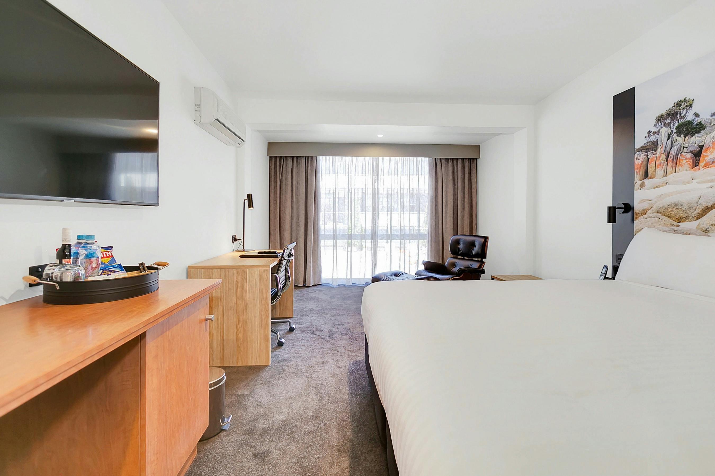 Guest accommodation room, with king bed, spacious with chair/footstool, work desk with chair, TV.