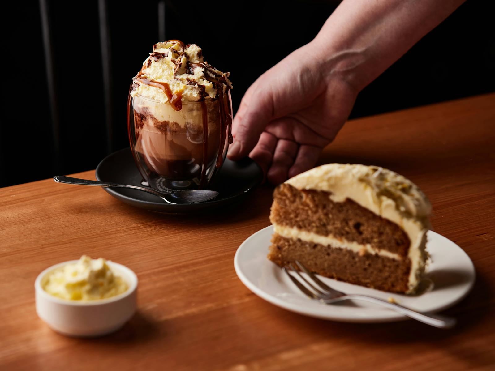 A carrot cakes topped with nuts and cream cheese sits in the foreground with a vienna coffee