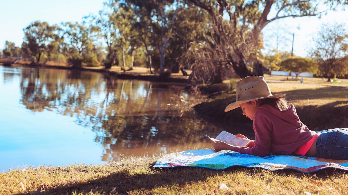 Young girl laying on a blanket, reading a book by the Yelarbon Lagoon