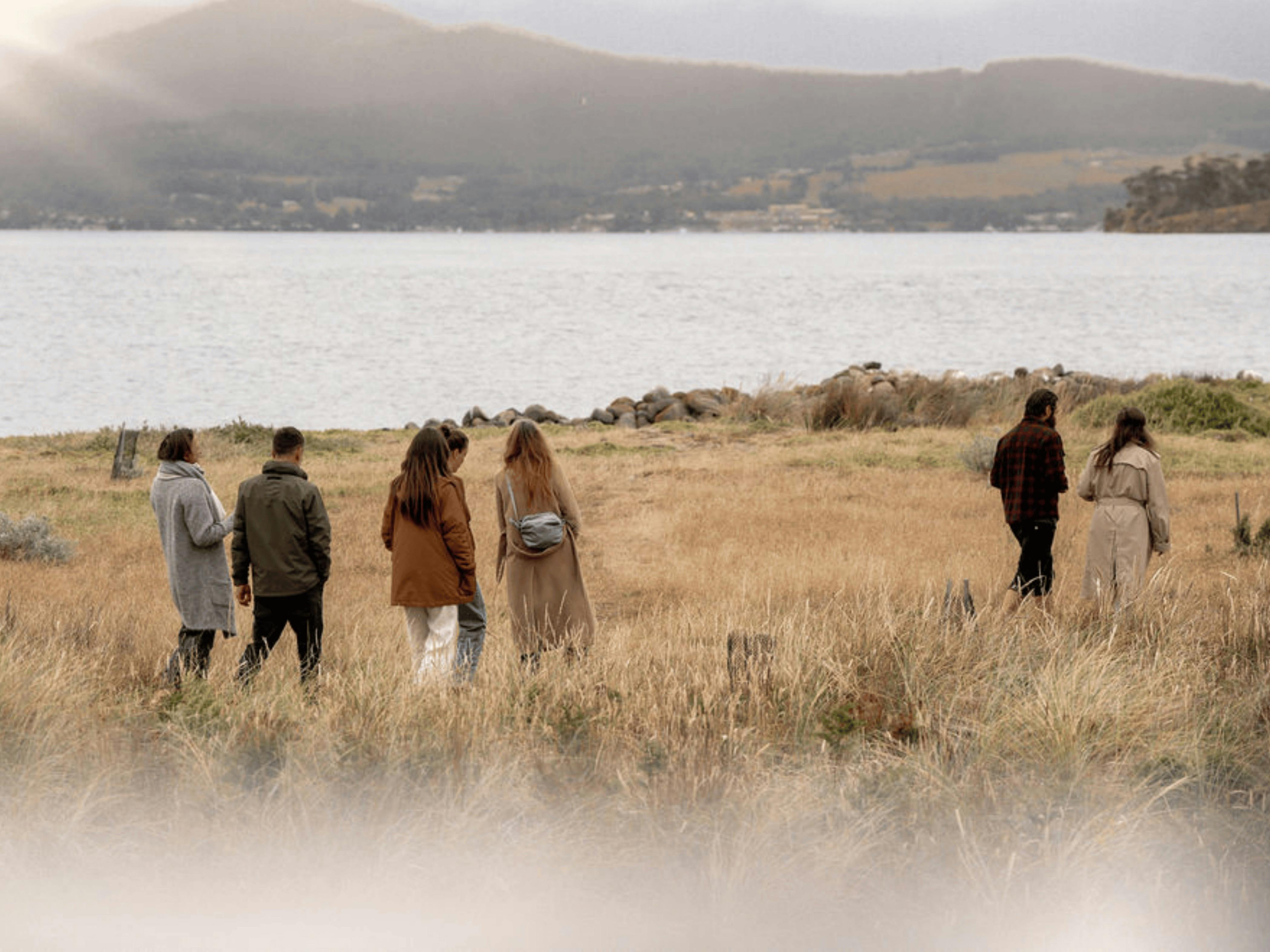 Group of six walking through coastal grassland toward the channel.