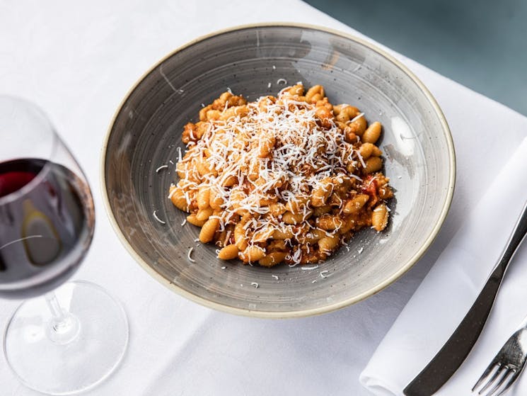 Bowl of pasta with red wine on a white table cloth.