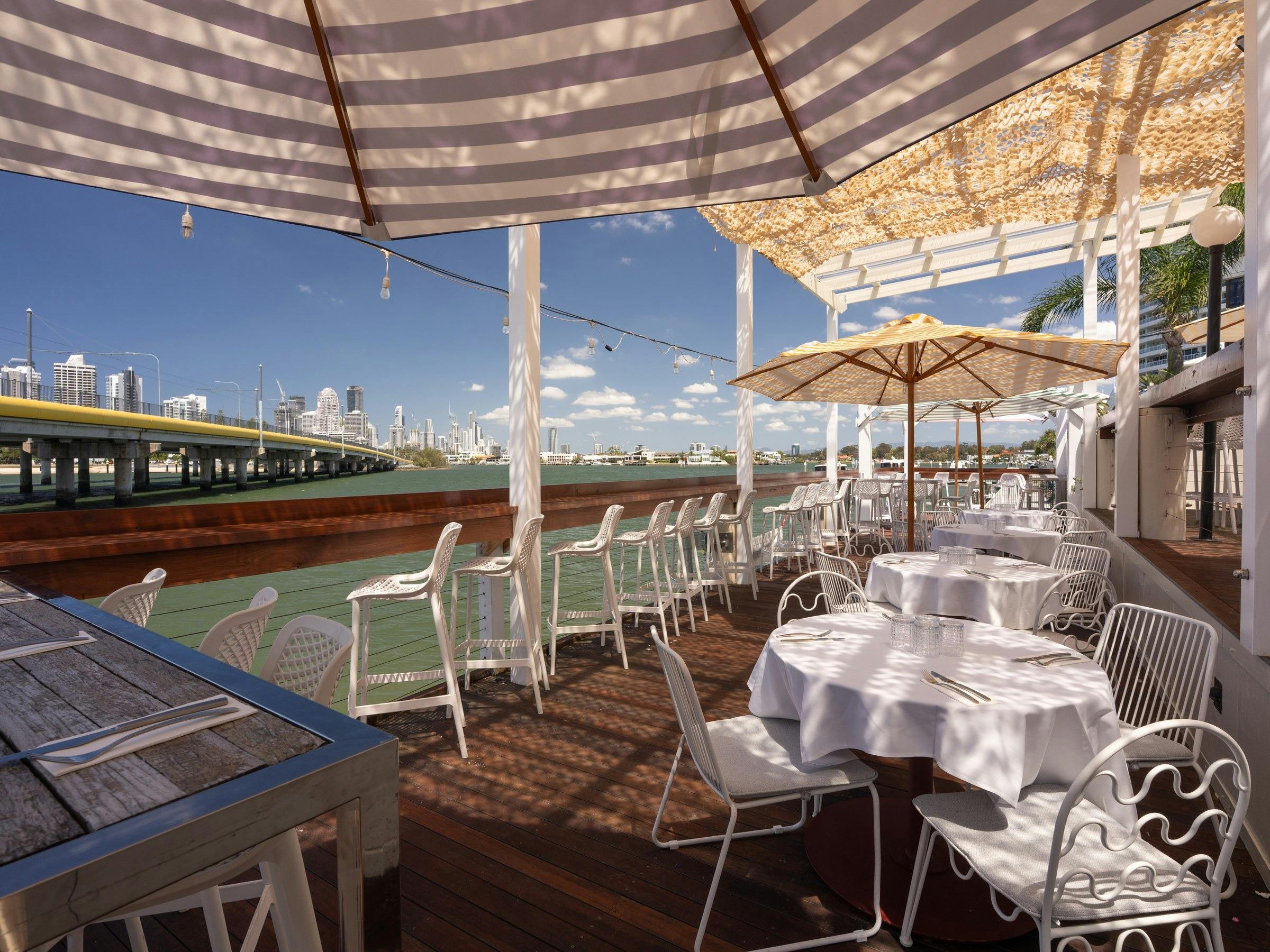 Riverside deck at River House with umbrellas and set tables overlooking the Gold Coast skyline