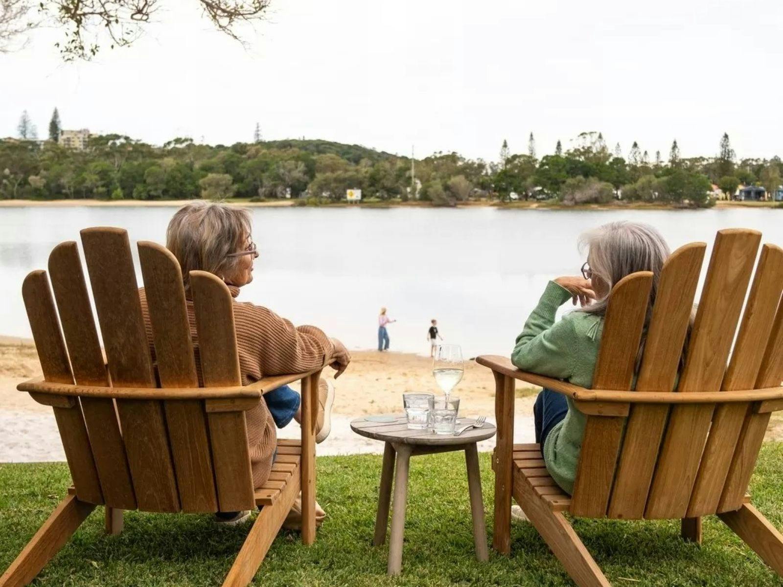 two ladies in large wooden chairs chatting and facing towards water