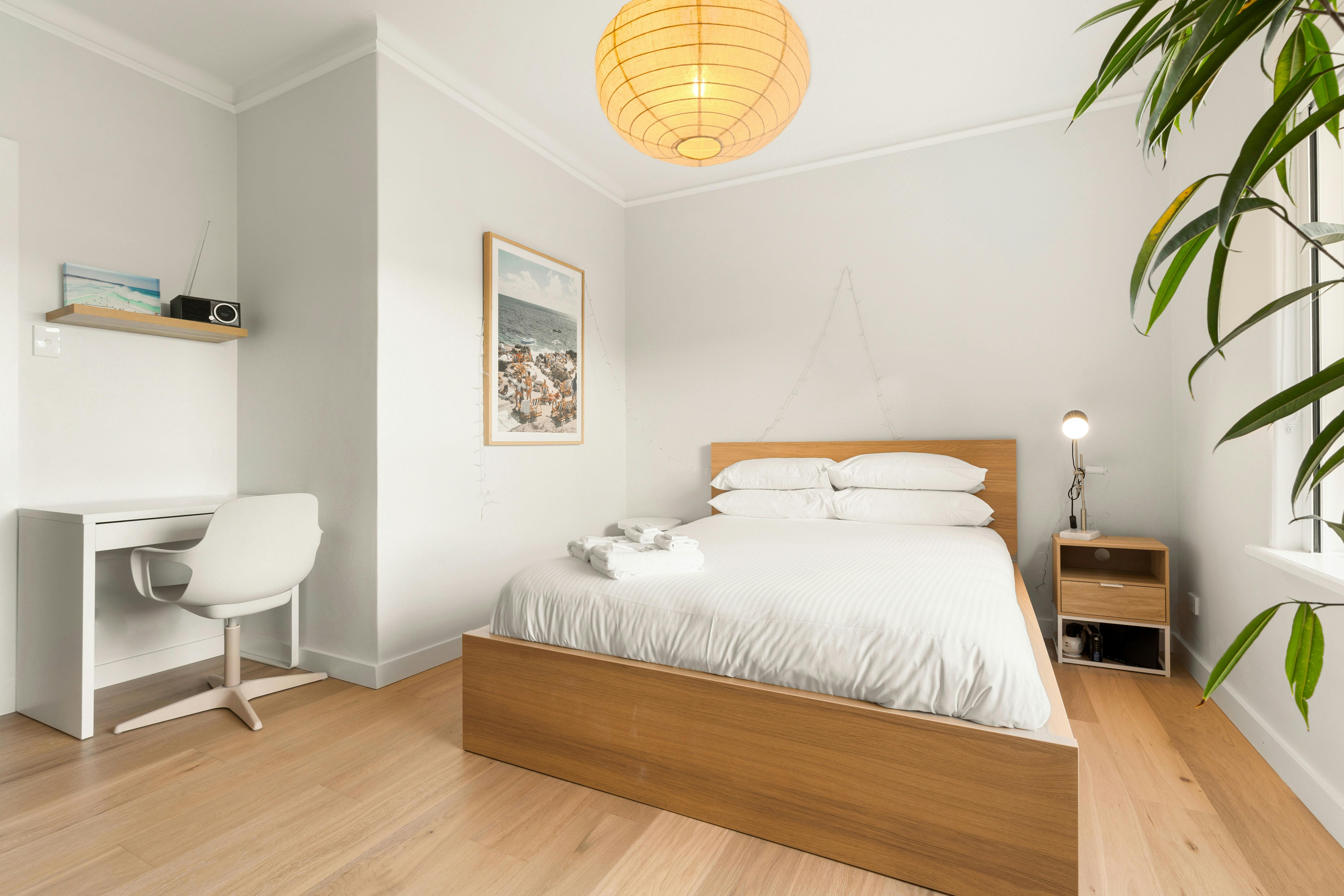 Bright and modern bedroom with a queen-sized bed, plant, and minimalistic decor.