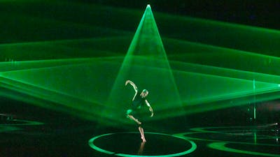 A dancer on stage with triangles of bright green light spotlighting