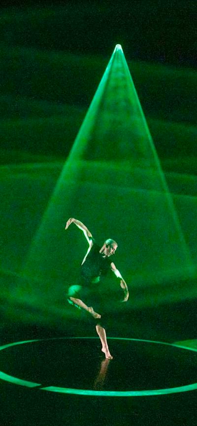 A dancer on stage with triangles of bright green light spotlighting