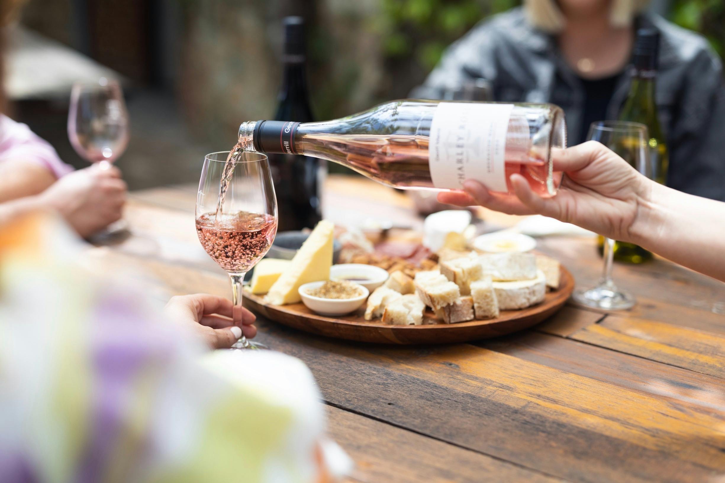 A glass of rosé wine being poured with a cheeseboard behind