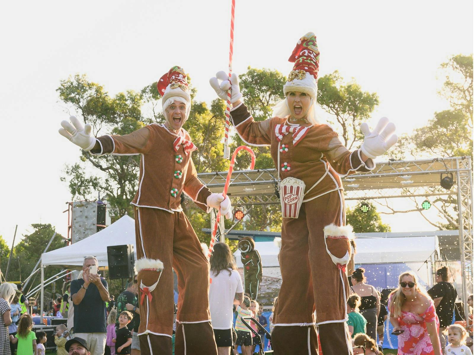 Two stiltwalkers dressed as gingerbread men waving to the camera