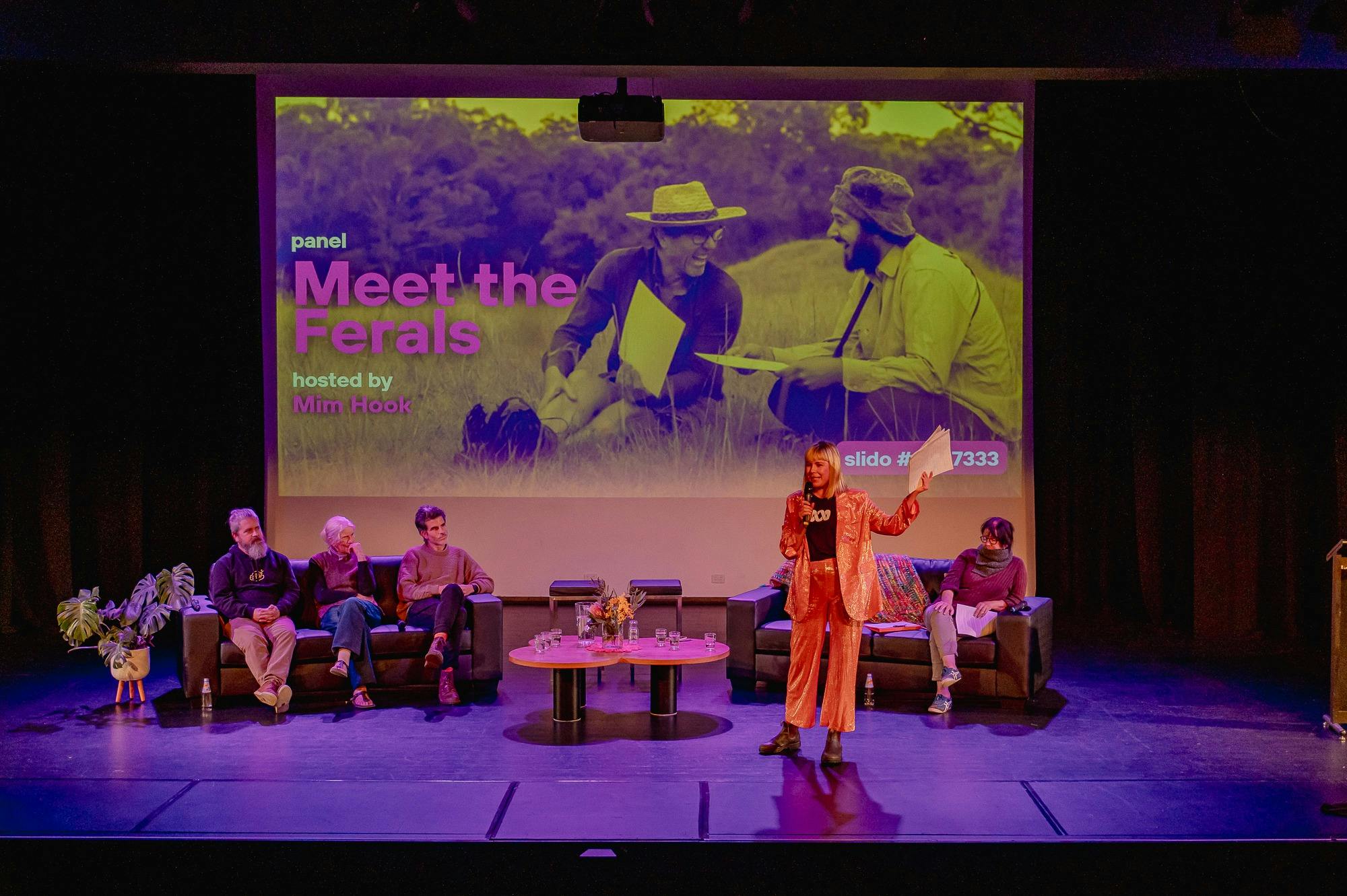 The words meet the ferals are on the screen as a panel sits and is being introduced by the mc