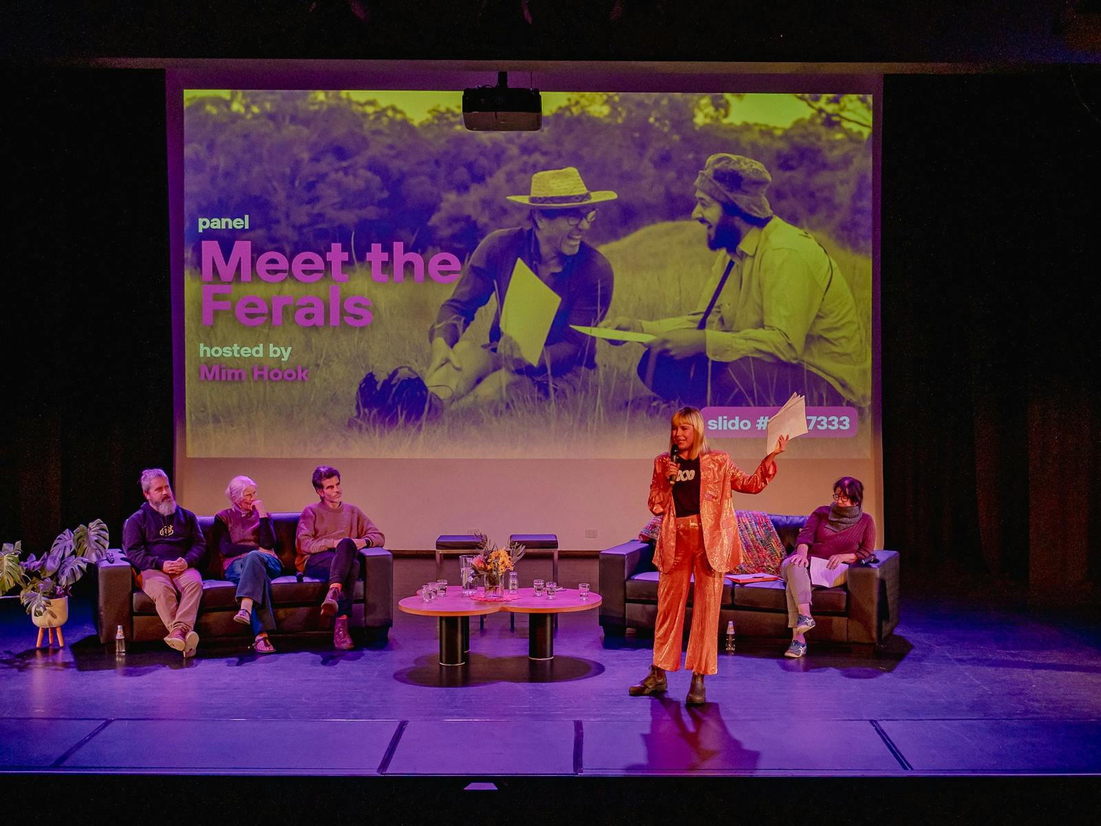 The words meet the ferals are on the screen as a panel sits and is being introduced by the mc