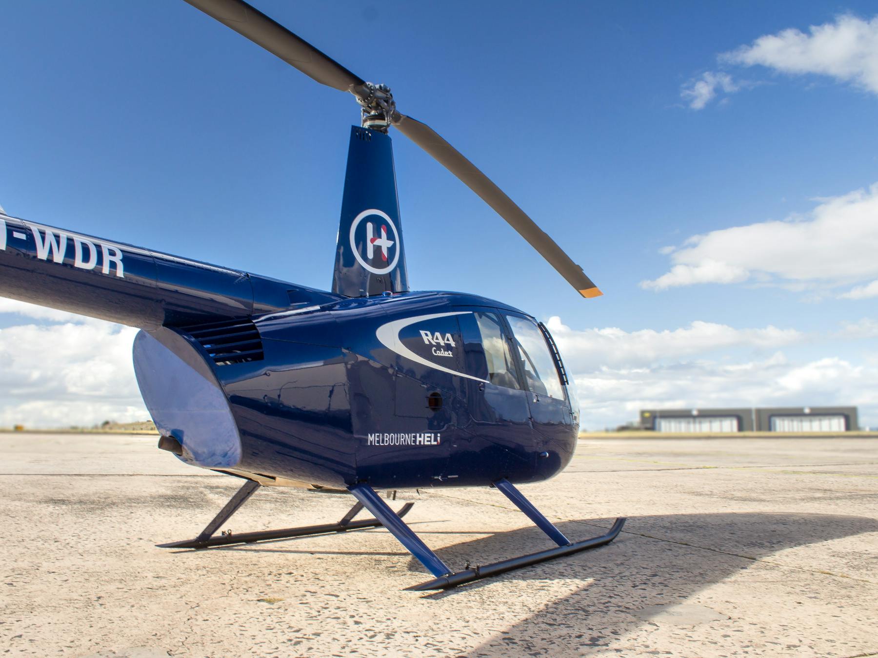 Blue Robinson R44 Cadet helicopter parked at the airport.