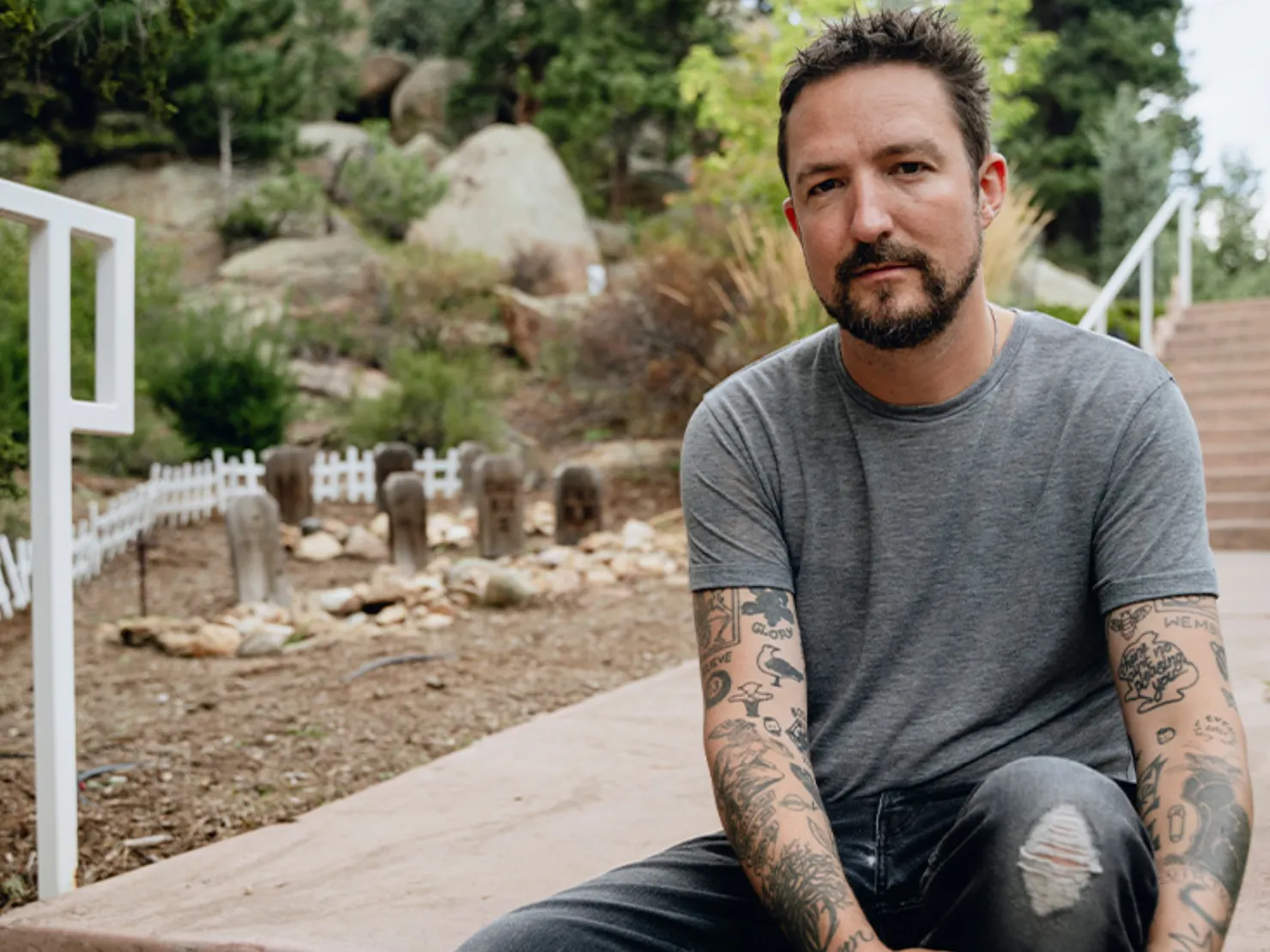 The member sitting outside on stairs with bush and plants surrounding him