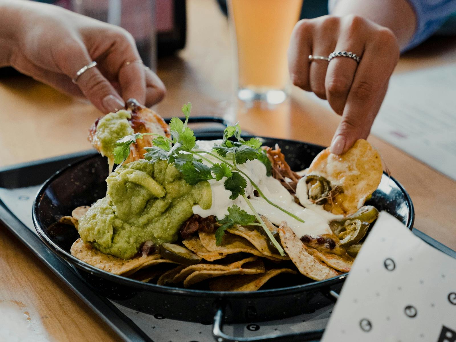 Hands picking up corn chips in a nachos dish