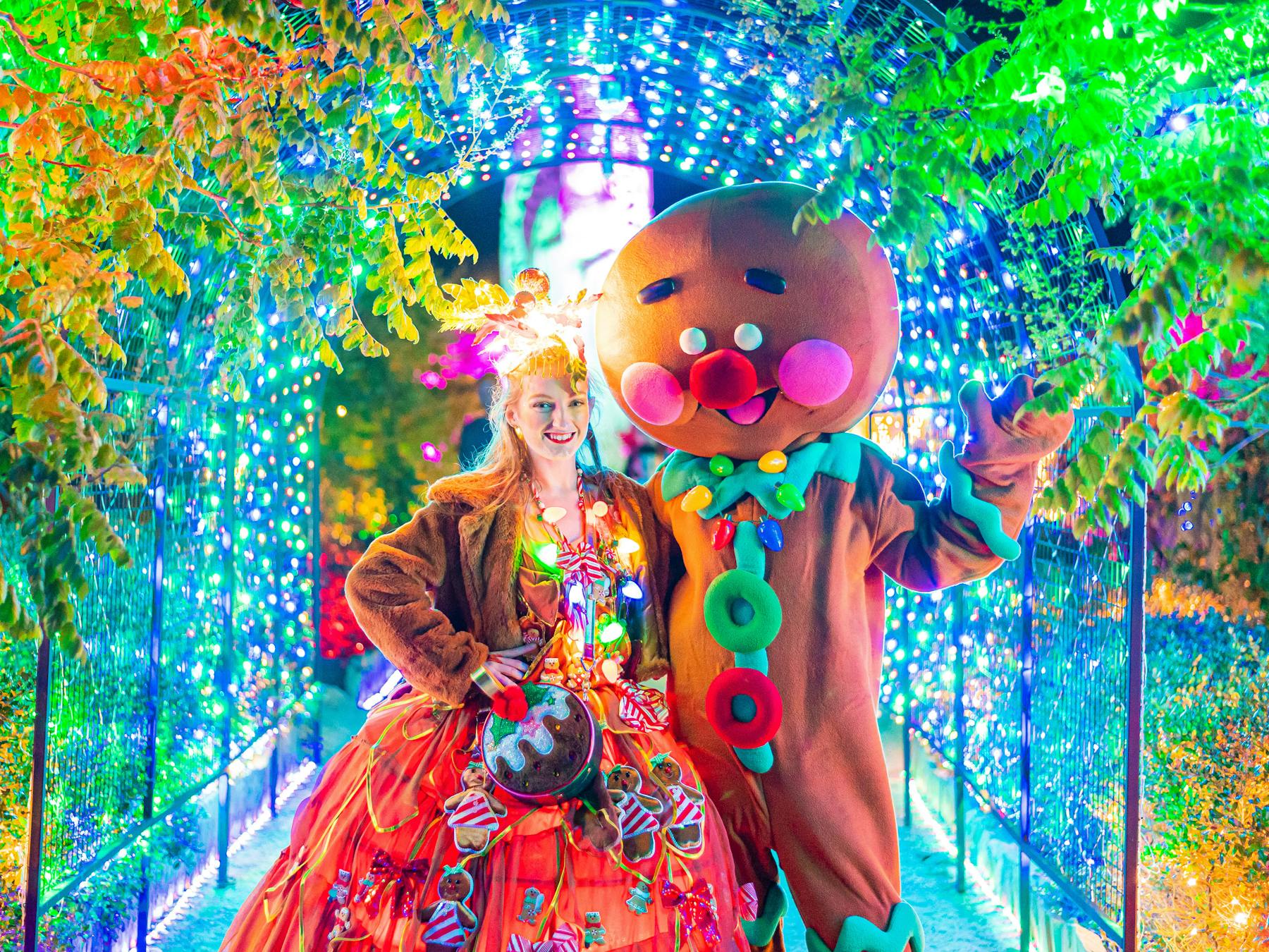woman in christmas outfit posing with gingerbread mascot surrounded by fairy lights in the garden