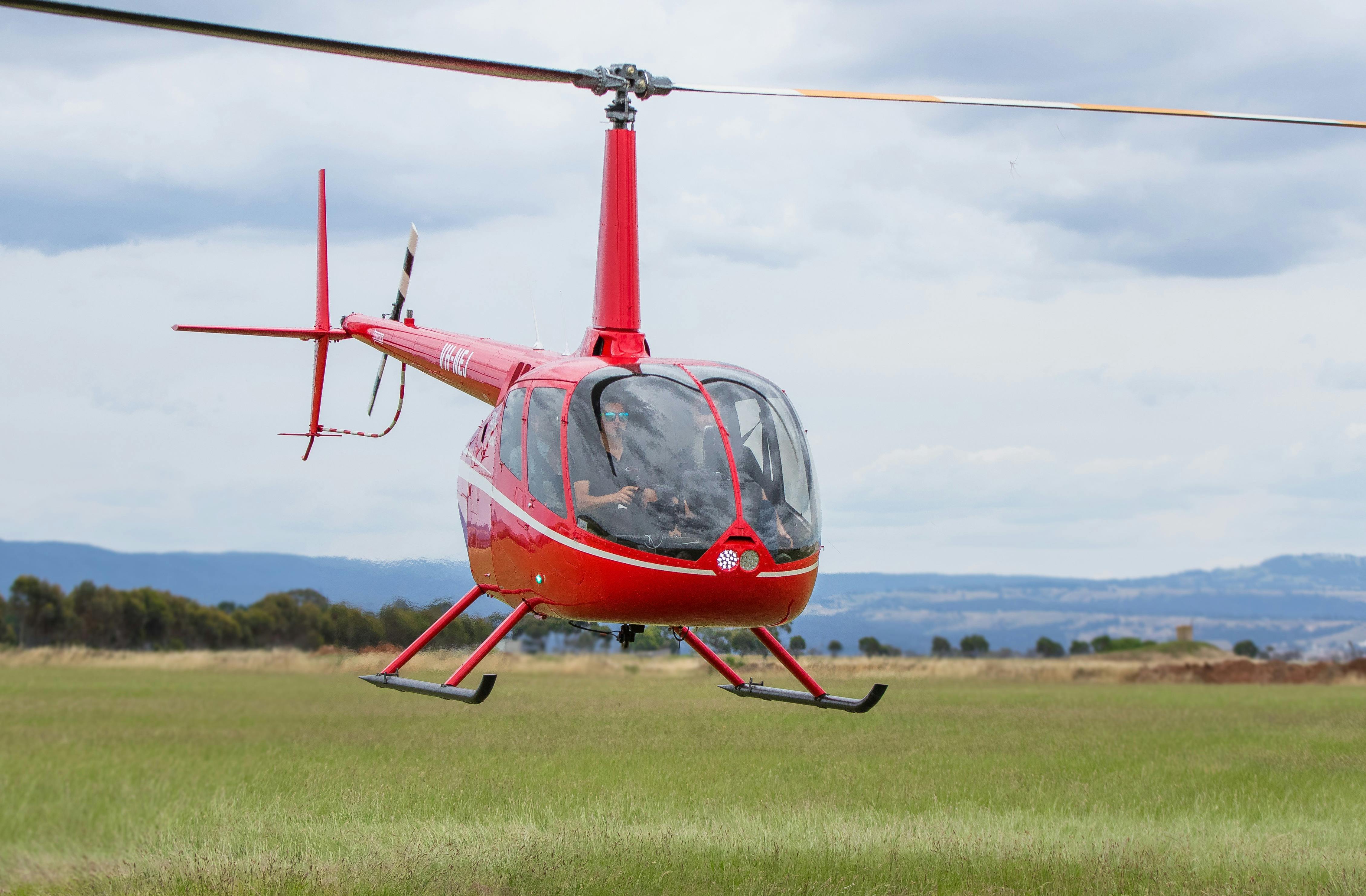 Red Robinson R66 Helicopter flying over green fields.