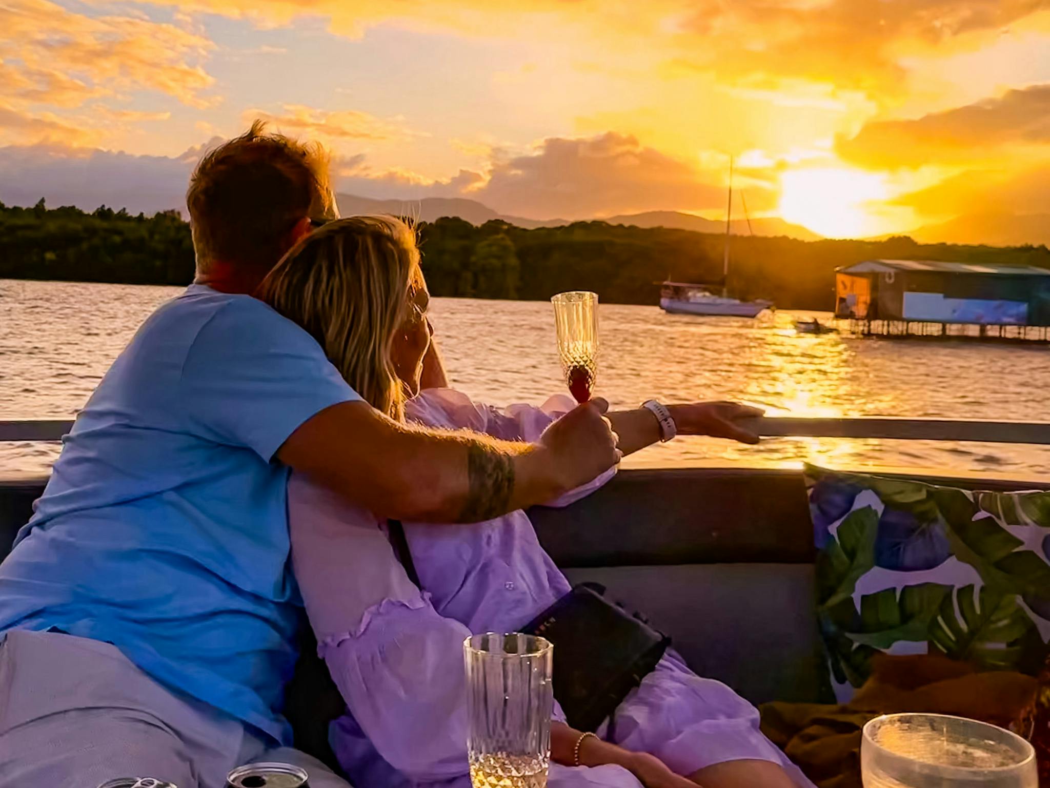 A couple embraced holding drinks and watching the sunset on the Cairns River Cruise A couple embraced holding drinks and watching the sunset on the Cairns River Cruise