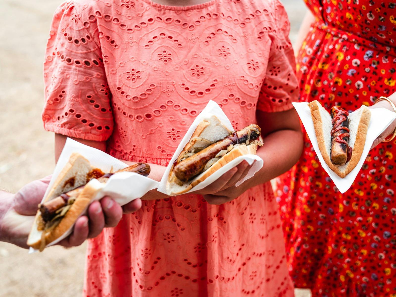 Image of people holding 3 sausage sandwhiches.