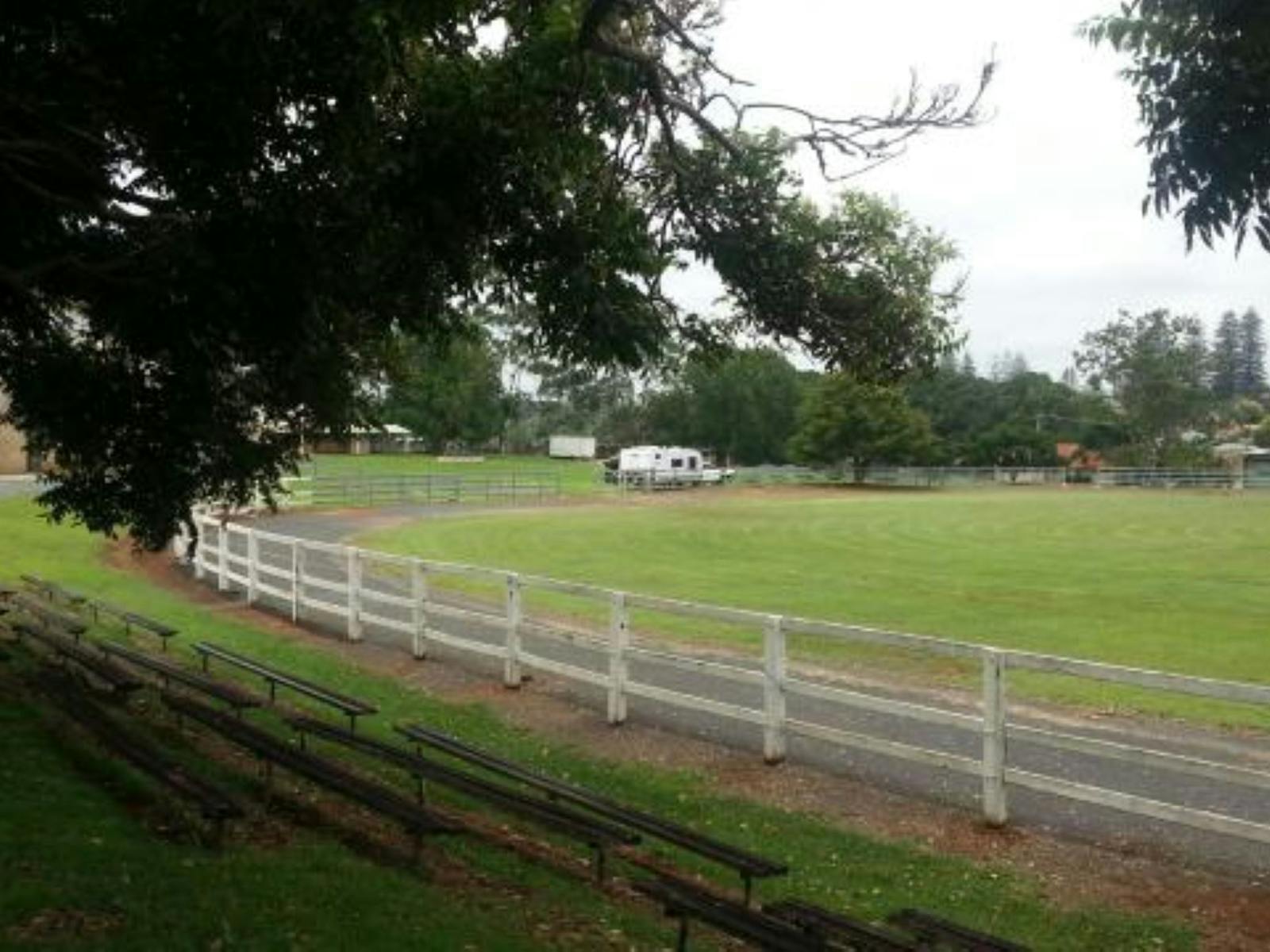 Image depicting a showground encircled by a white fence with a camper trailer parked in the centre