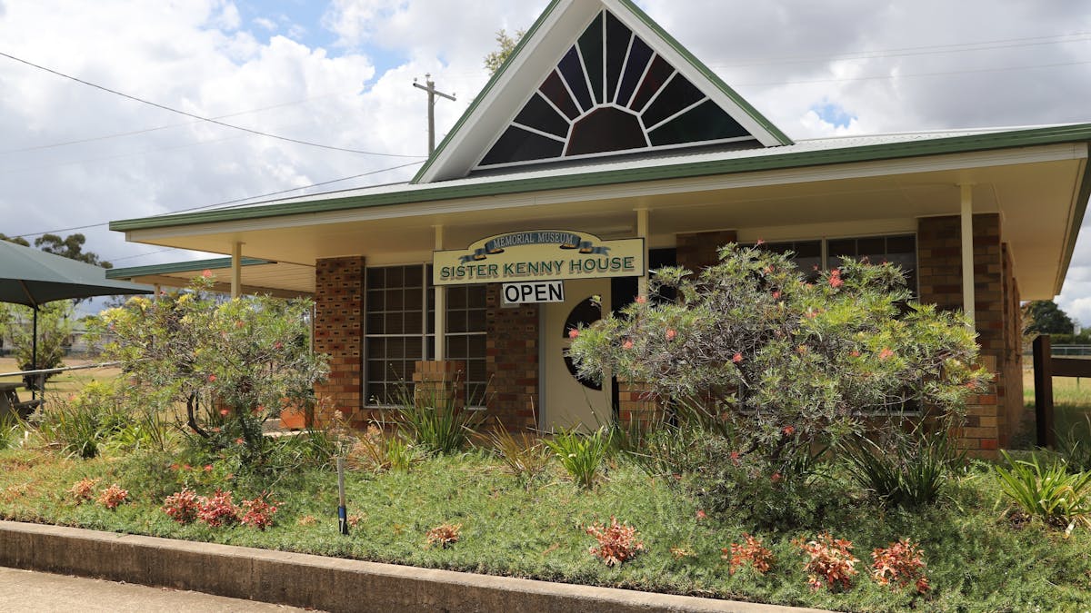 Small brick building surrounded by garden which sign at front stating Sister Kenny Memorial House