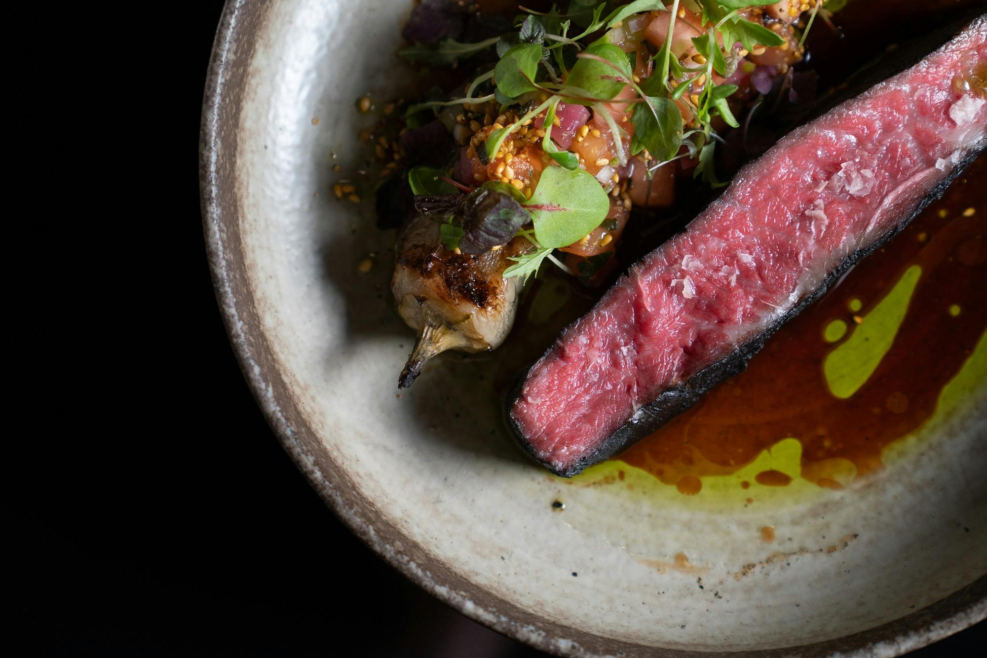 Sliced Mayura Wagyu beef with vegetables and sauce on a ceramic plate