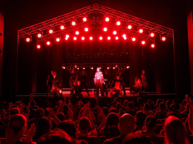 Jo stands centre stage with red lighting and audience cheering