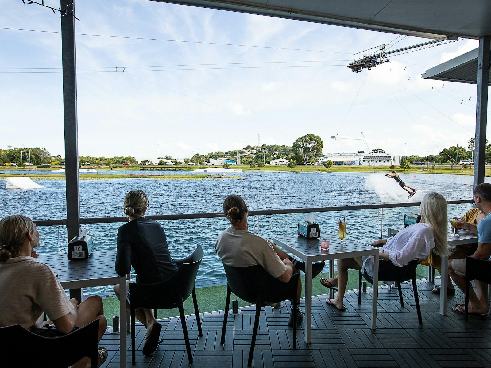 Customers enjoying a drink, relaxing, watching the wakeboarding lake from the cafe deck. Customers enjoying a drink, relaxing, watching the wakeboarding lake from the cafe deck.