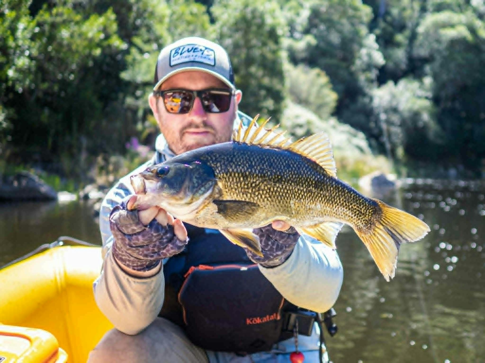 A man holding an Australian Bass in a yellow raft on the Snowy River