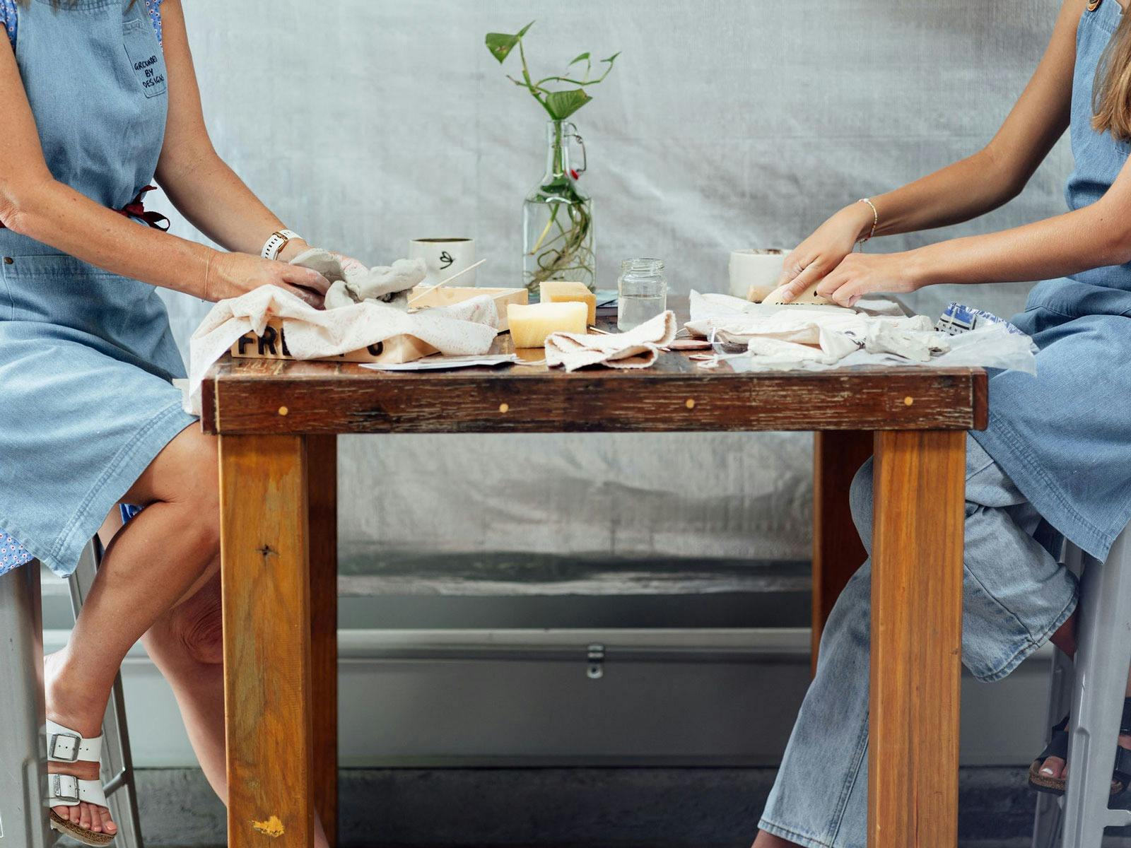 2 women playing with clay at a wooden coffee table with tools nearby