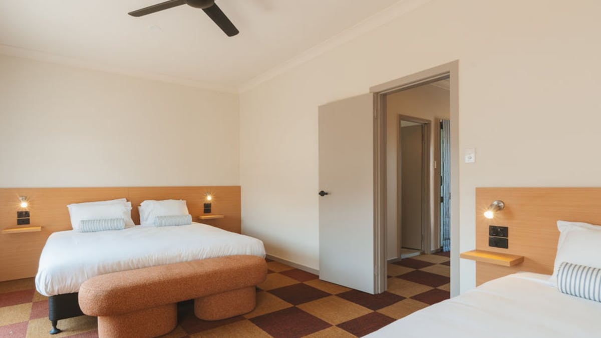 Spacious hotel room with two beds, warm timber furnishings and checkered flooring at Hotel Allen.
