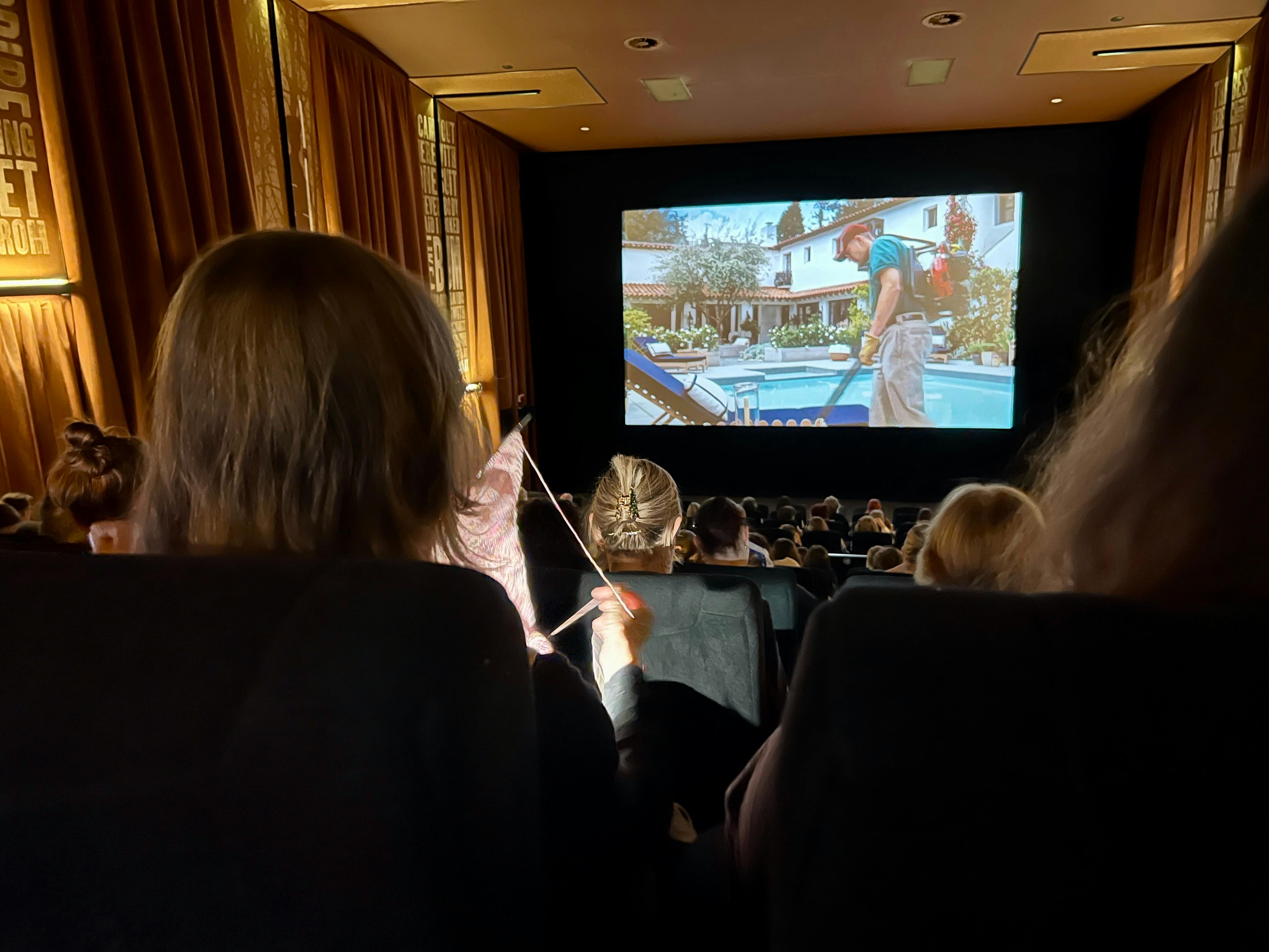 View from the back of a cinema, showing audience members watching a film on a large screen while a p