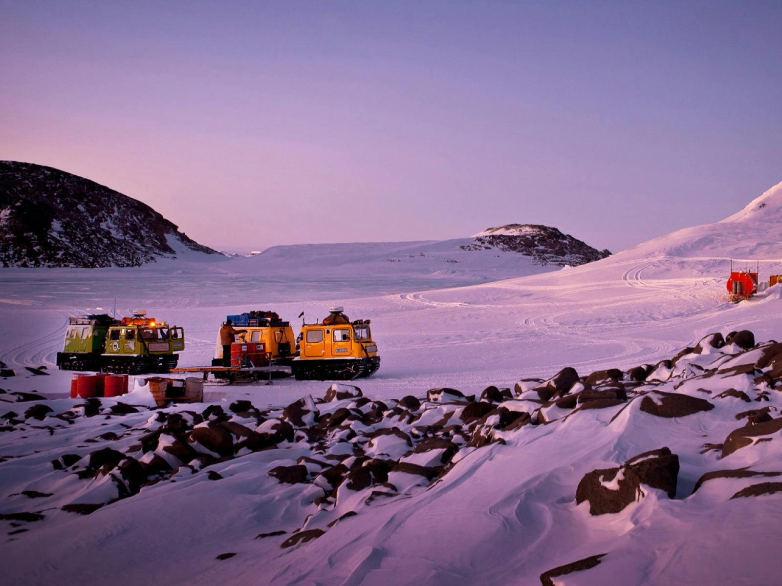 Two Hägglunds in evening light at a field hut in a serene snowy landscape.