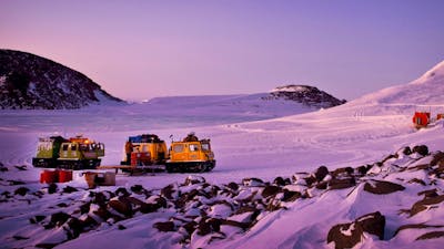 Two Hägglunds in evening light at a field hut in a serene snowy landscape.