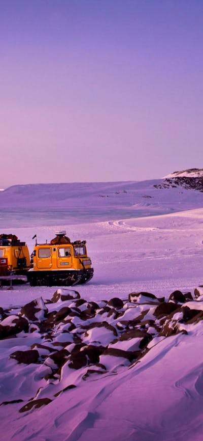Two Hägglunds in evening light at a field hut in a serene snowy landscape.