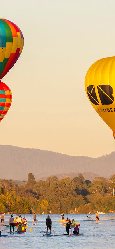 Four floating hot air balloons over lake in Canberra