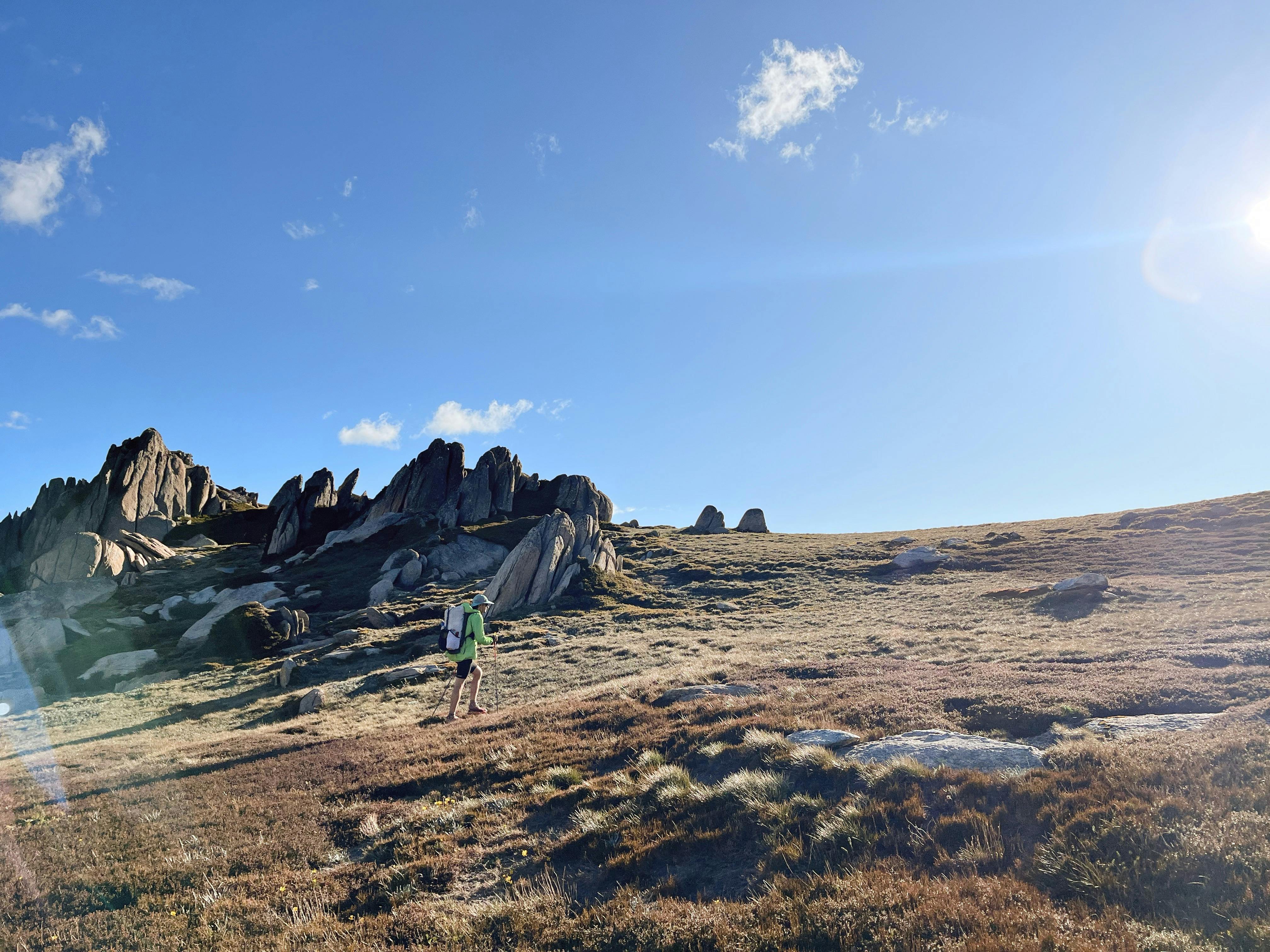 A hiker walking up a slope in the mountains with some jagged rocks behind them.