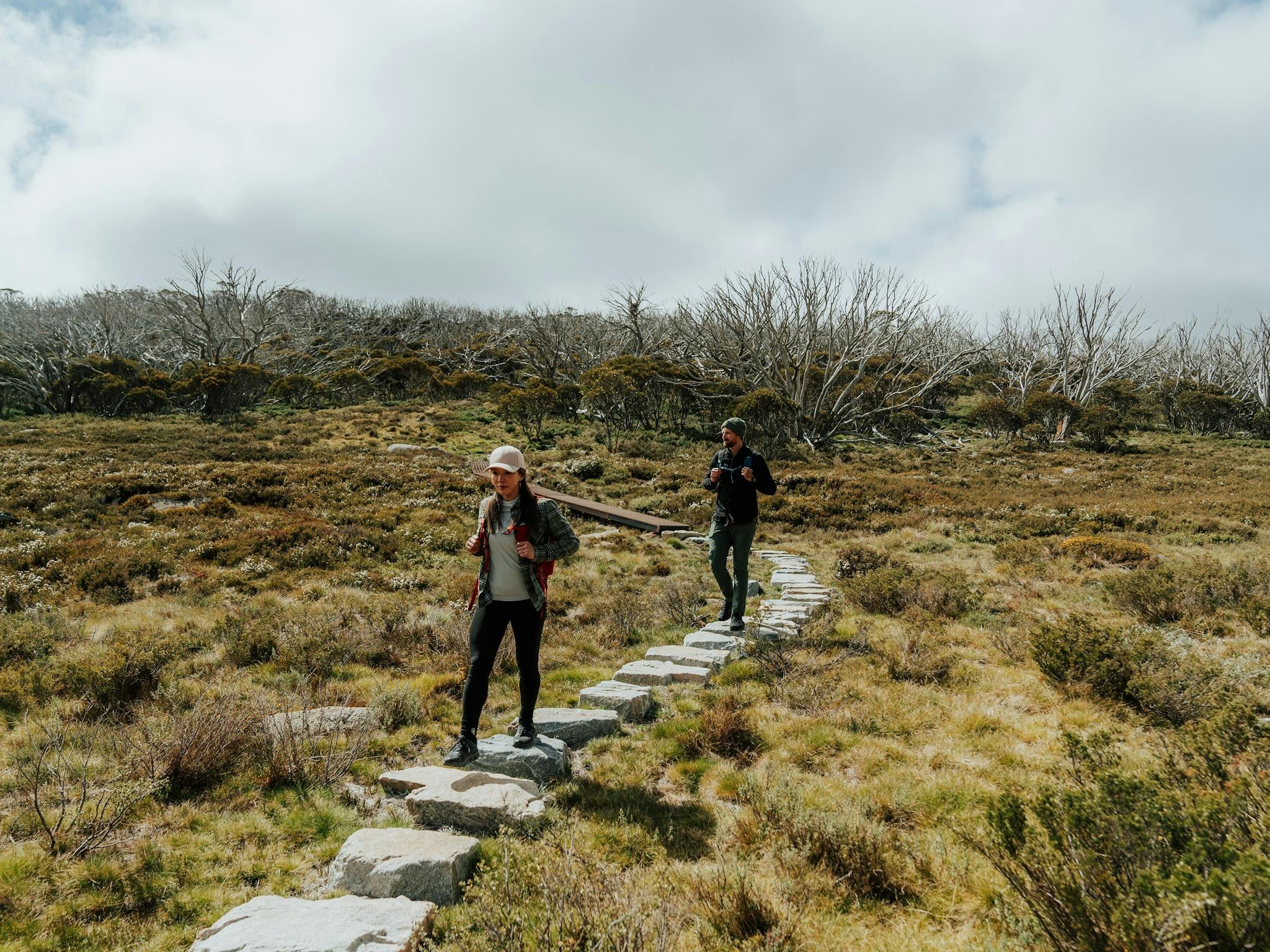 Two hikers crossing a stone section of track on a walk in Kosciuszko National Park.