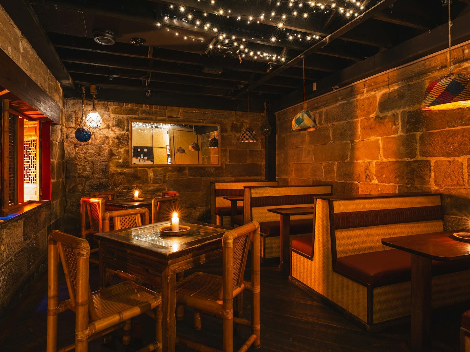 Warm lounge with stone walls, bamboo chairs, booth seating, hanging lamps, and fairy lights