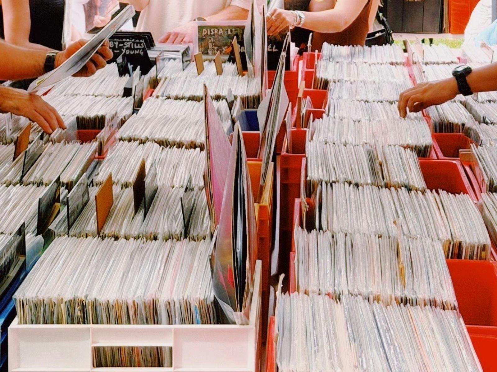 People browse through rows of vinyl records organized in bins at an outdoor market