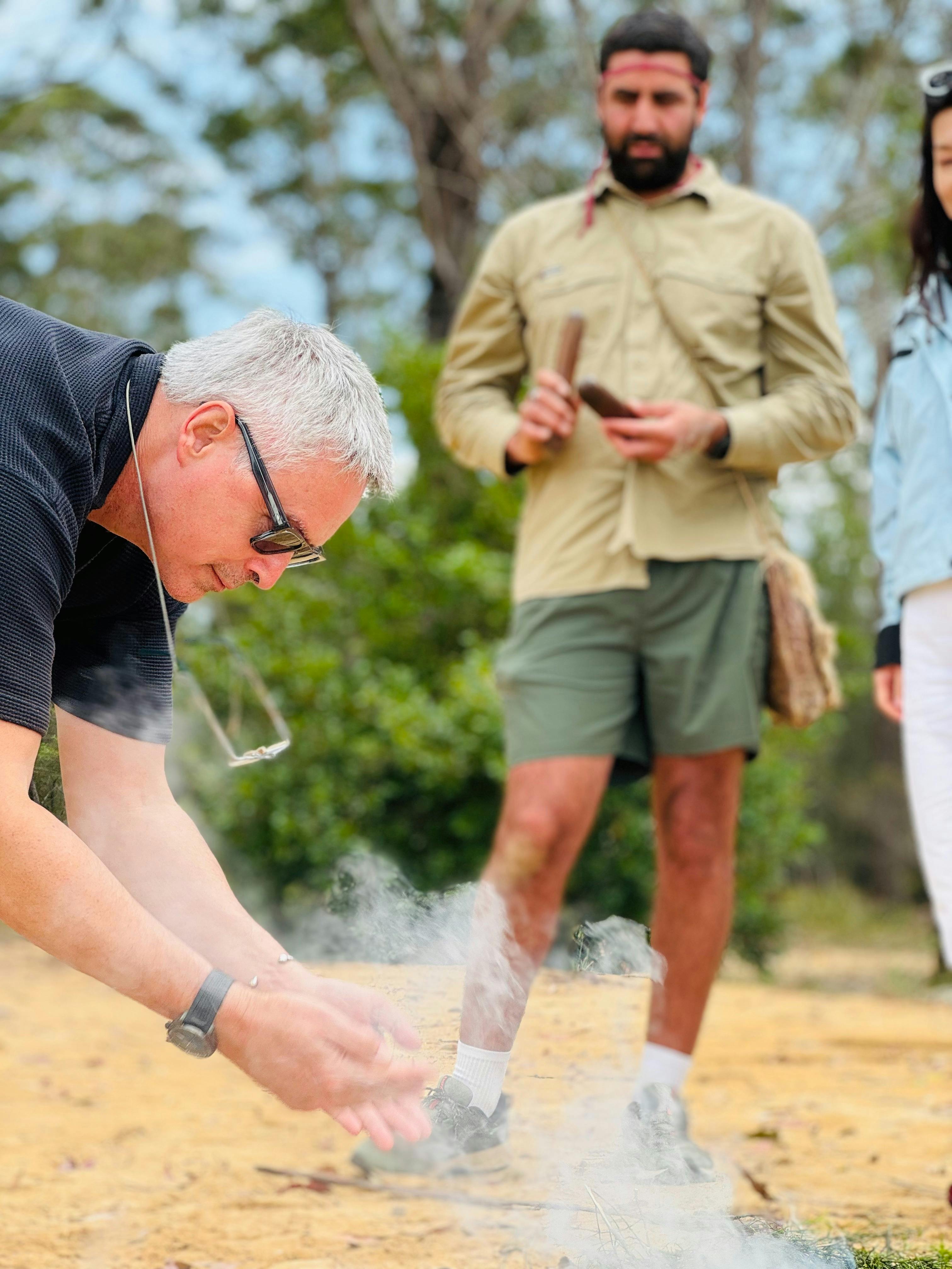Man leans down and waves smoke closer to him as Country Custodian looks on