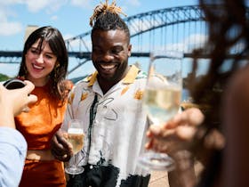 A man and  woman enjoy bubbles on a balcony in front of the Sydney Harbour Bridge