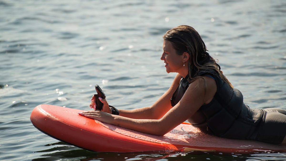 Girl on pink Fliteboard in the water looking at the controller . Learn to foil Noosa