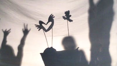 Shadow puppets move across a screen as the outlines of children dancing are visible on either side