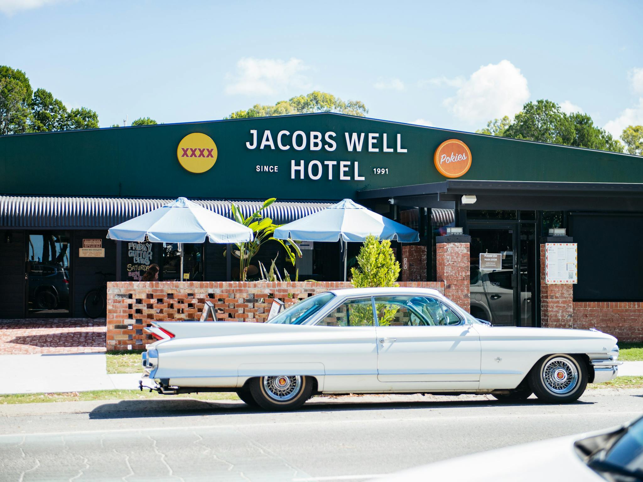 A vintage white Cadillac parked in front of the dark green Jacobs Well Hotel building on a sunny day A vintage white Cadillac parked in front of the dark green Jacobs Well Hotel building on a sunny day