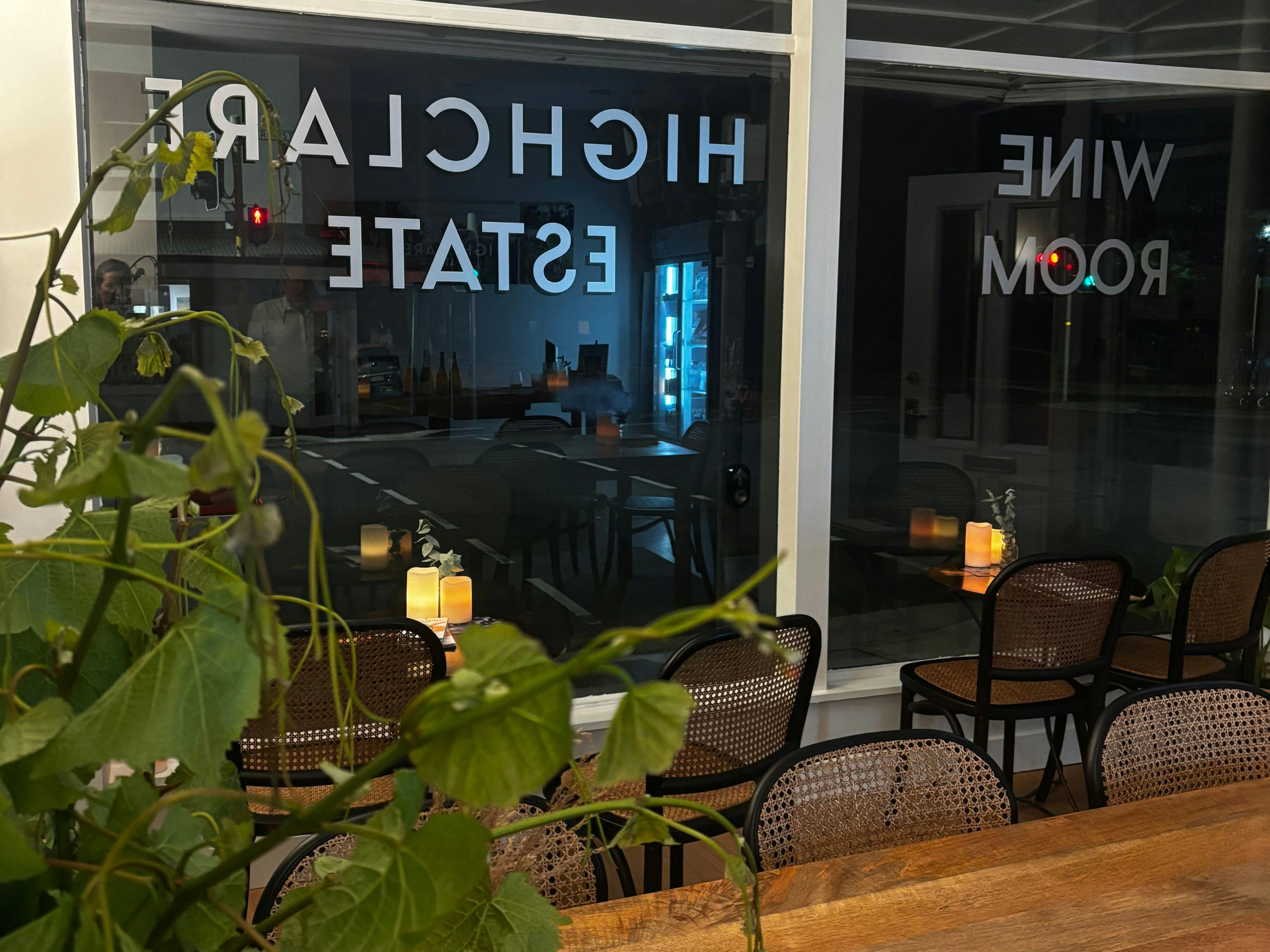 Foreground has cuttings of grape vines sitting on group table, night time view, window signage rev