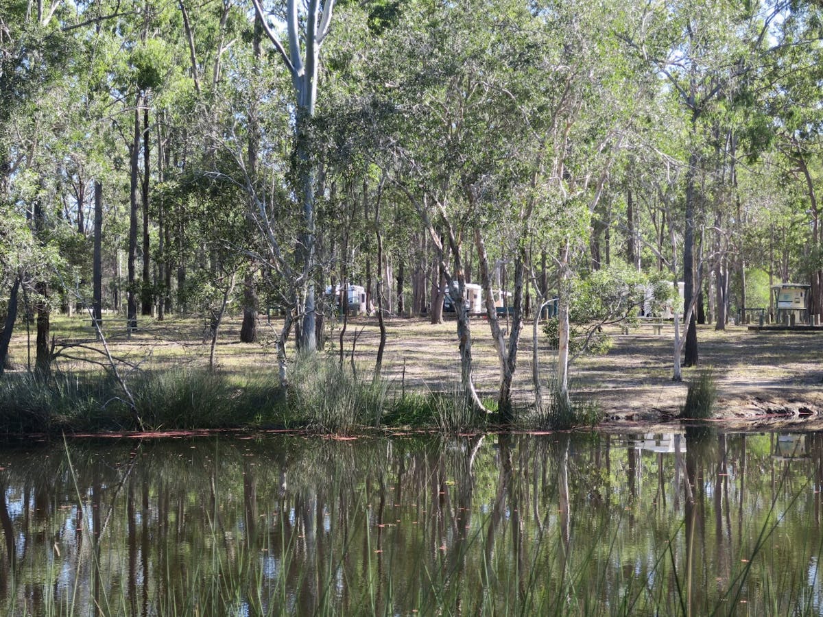 Looking across waterhole at camping area with two caravans.