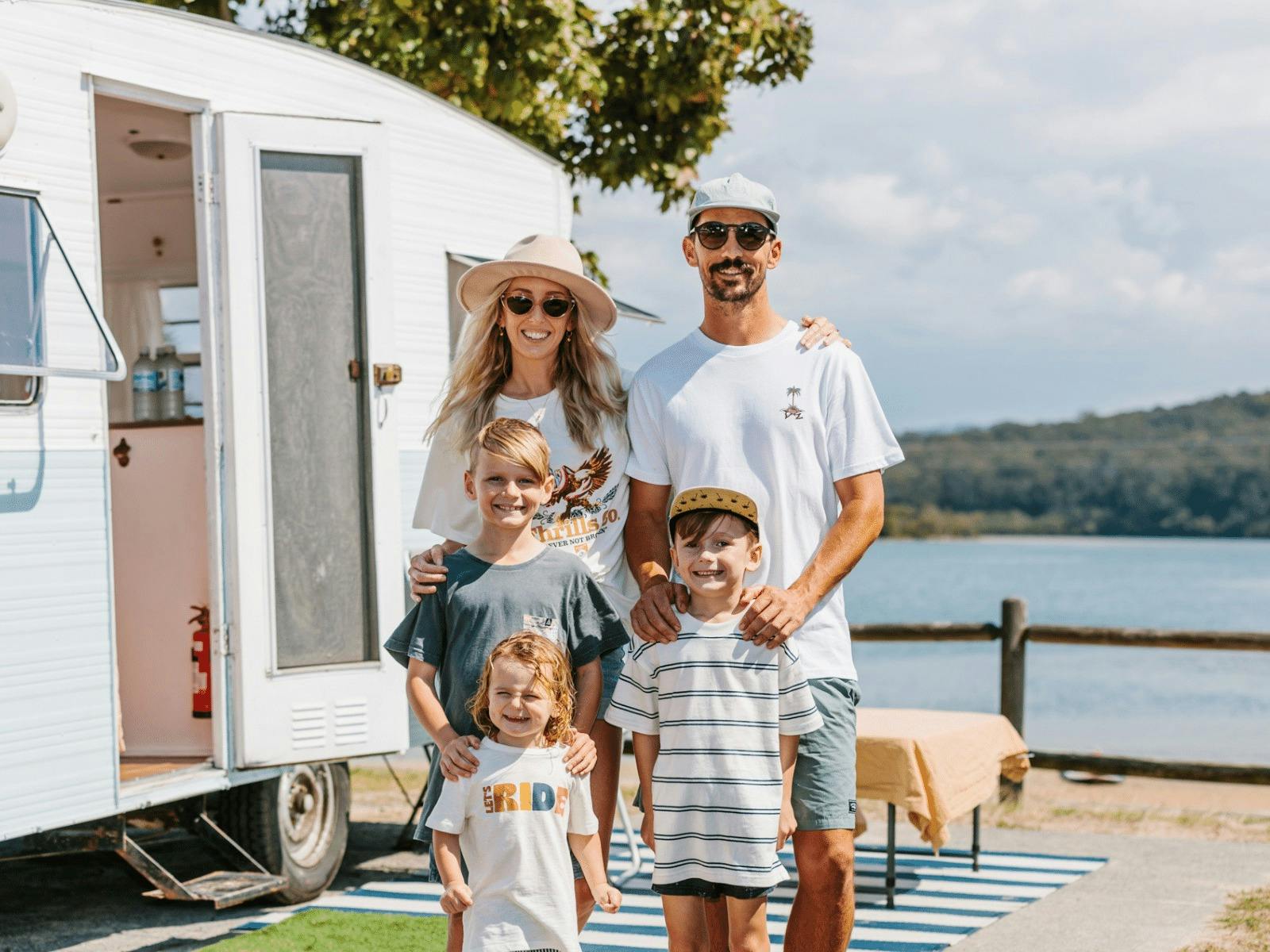 Family of four in front of vintage caravan with lake in the background Family of four in front of vintage caravan with lake in the background