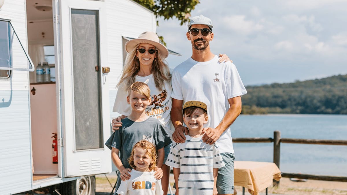 Family of four in front of vintage caravan with lake in the background